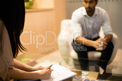 Businesswoman writing on clipboard while discussing with male colleague