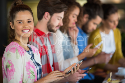 Portrait of smiling woman holding mobile phone while sitting with friends
