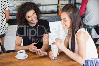 Smiling couple using mobile phone while having drinks in restaurant
