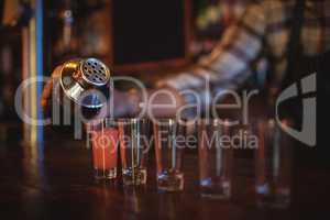 Waiter pouring cocktail drink into shot glasses at counter