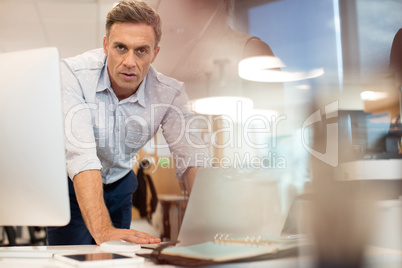 Portrait of businessman working on laptop while leaning at desk