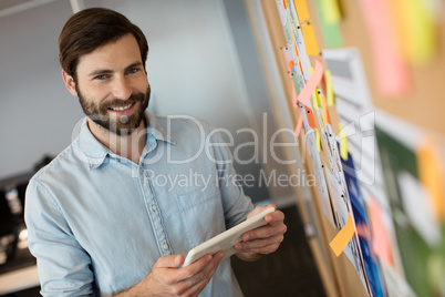Portrait of young businessman holding digital tablet by soft board