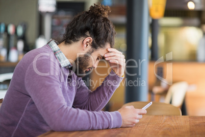 Depressed man holding mobile phone in restaurant