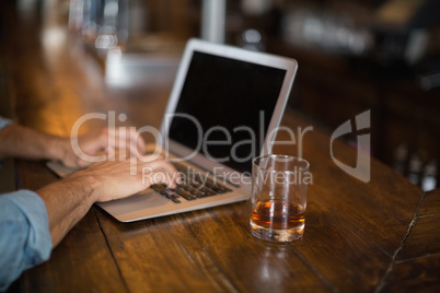Cropped hands using laptop by beer glass at pub