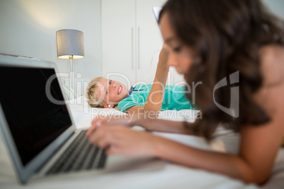 Siblings using digital tablet and laptop on bed