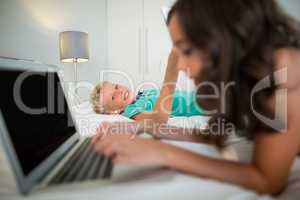 Siblings using digital tablet and laptop on bed