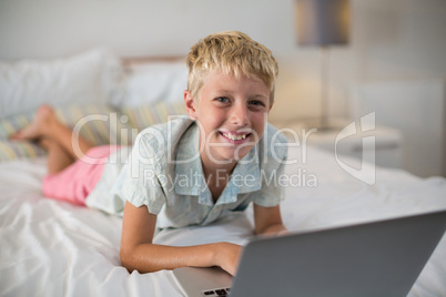 Portrait of smiling boy using laptop on bed in bedroom