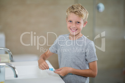 Portrait of boy putting toothpaste on brush in bathroom