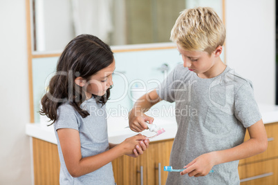 Boy putting toothpaste on sister toothbrush in bathroom
