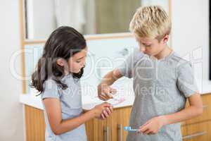 Boy putting toothpaste on sister toothbrush in bathroom
