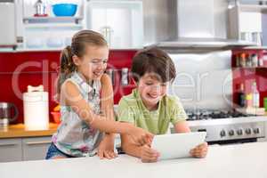 Happy siblings using digital tablet in kitchen