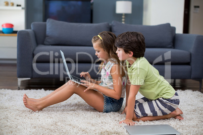 Siblings using laptop in living room