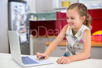 Smiling girl using laptop in kitchen