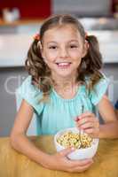 Portrait of smiling girl having breakfast cereal in kitchen