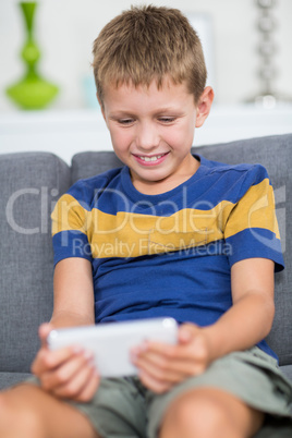 Happy boy sitting on sofa and using mobile phone in living room