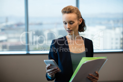 Businesswoman using mobile phone while holding files