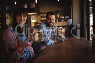 Portrait of happy couple holding glasses of beer at counter