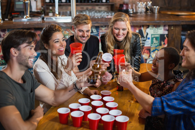 Happy friends drinking beer while sitting around disposable cups in bar