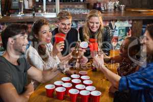 Happy friends drinking beer while sitting around disposable cups in bar