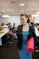 Businesswoman using mobile phone while holding exercise mat