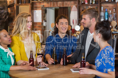 Young friends talking while standing by digital tablets and beer bottles in pub