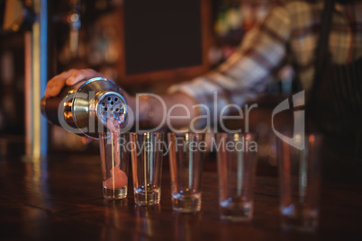 Waiter pouring cocktail drink into shot glasses at counter