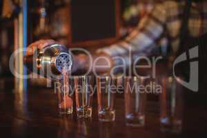 Waiter pouring cocktail drink into shot glasses at counter