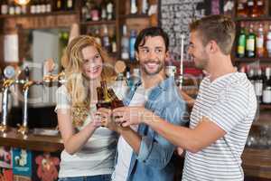 Cheerful friends toasting beer bottles at pub
