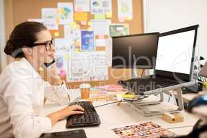 Businesswoman using mobile phone while typing on computer