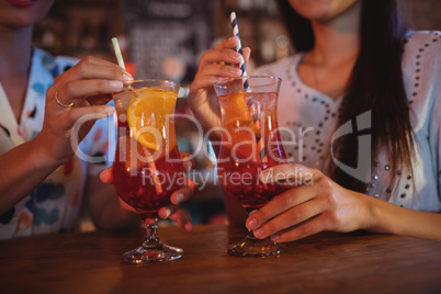 Mid-section of two young women having cocktail drinks