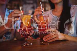 Mid-section of two young women having cocktail drinks