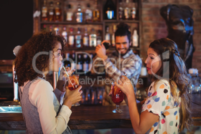 Two young women having cocktail drinks at counter