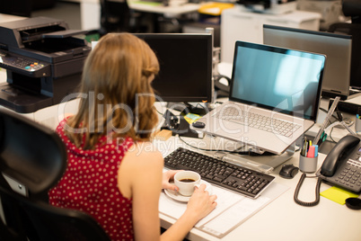 Businesswoman having coffee while working in office