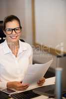 Portrait of smiling businesswoman holding documets at desk