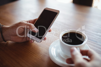 Hands of man using mobile phone while having coffee