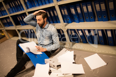 Tired businessman with scattered papers in file storage room