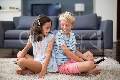 Siblings sitting on rug and using digital tablet in living room