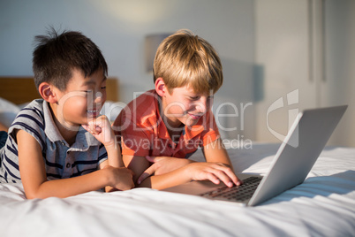 Smiling siblings using laptop on bed