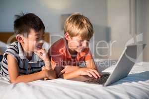 Smiling siblings using laptop on bed