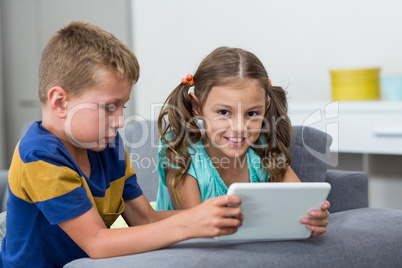 Siblings using digital tablet in living room