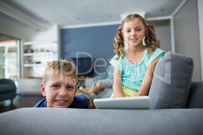 Portrait of siblings with digital tablet sitting on sofa in living room