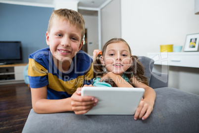 Portrait of siblings with digital tablet sitting on sofa in living room