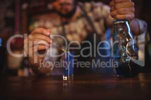 Waiter pouring cocktail drink into shot glasses at counter