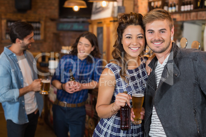 Smiling friends holding beer glass and bottle in pub