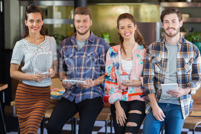 Friends posing with mobile phones and digital tablets in restaurant