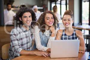 Smiling friends using laptop while sitting in restaurant