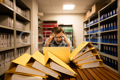 Worried businessman with laptop in file storage room