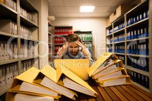 Worried businessman with laptop in file storage room