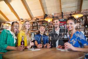 Portrait of friends holding beer bottles and wine glasses on table