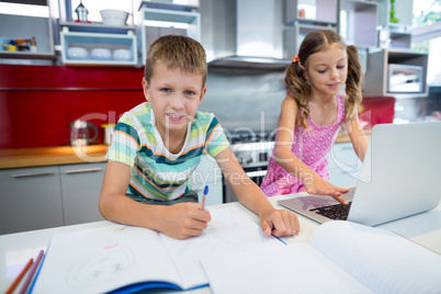 Boy doing his homework while girl using laptop in kitchen